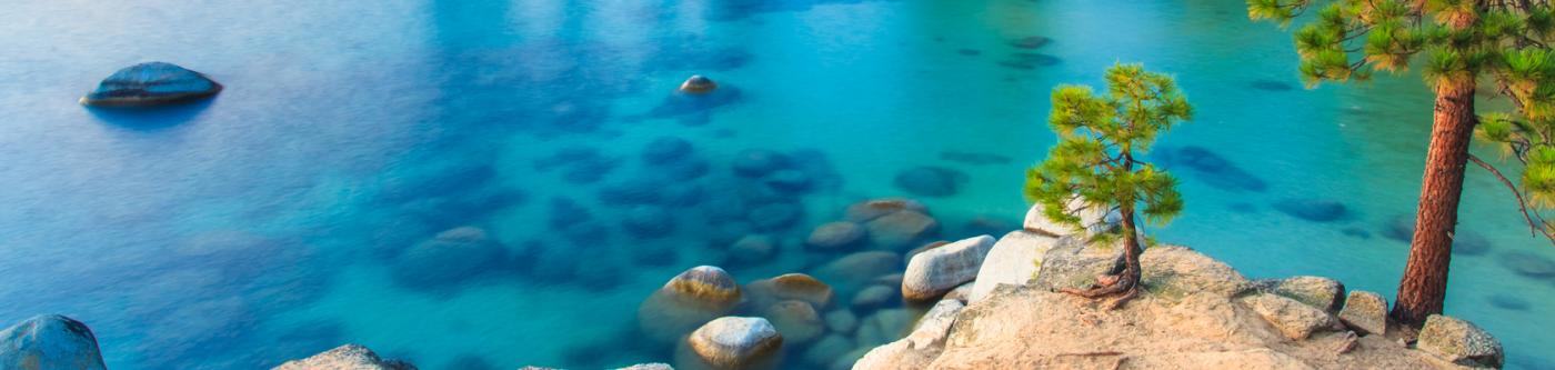 Clear blue lake with visible rocks on the bottom and trees on the right.