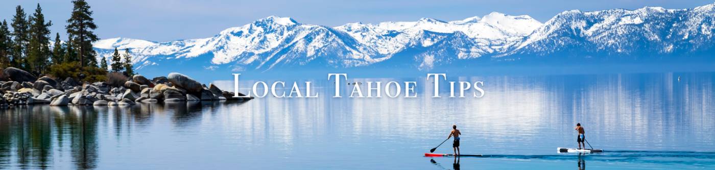 Two men paddle boarding on Lake Tahoe with snowcapped mountains in the background.