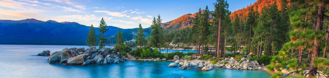 Lake Tahoe coast at dusk with rocks and trees along the edge.