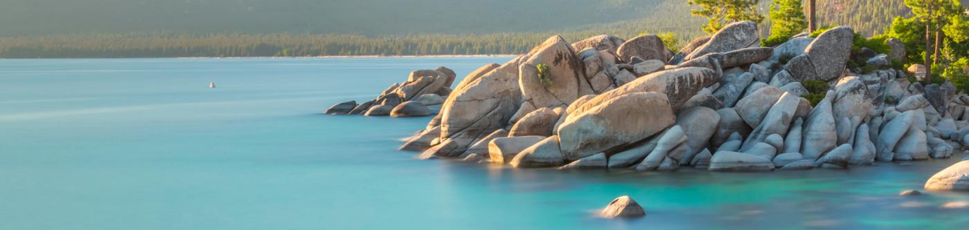Large rocks on the coast of a Lake Tahoe cove with trees on the right side.